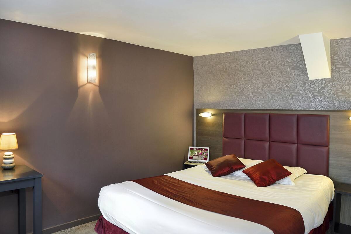 Una habitación de hotel con una cama grande, una mesita de noche con lámpara, un ordenador portátil y un panel decorativo en la pared.