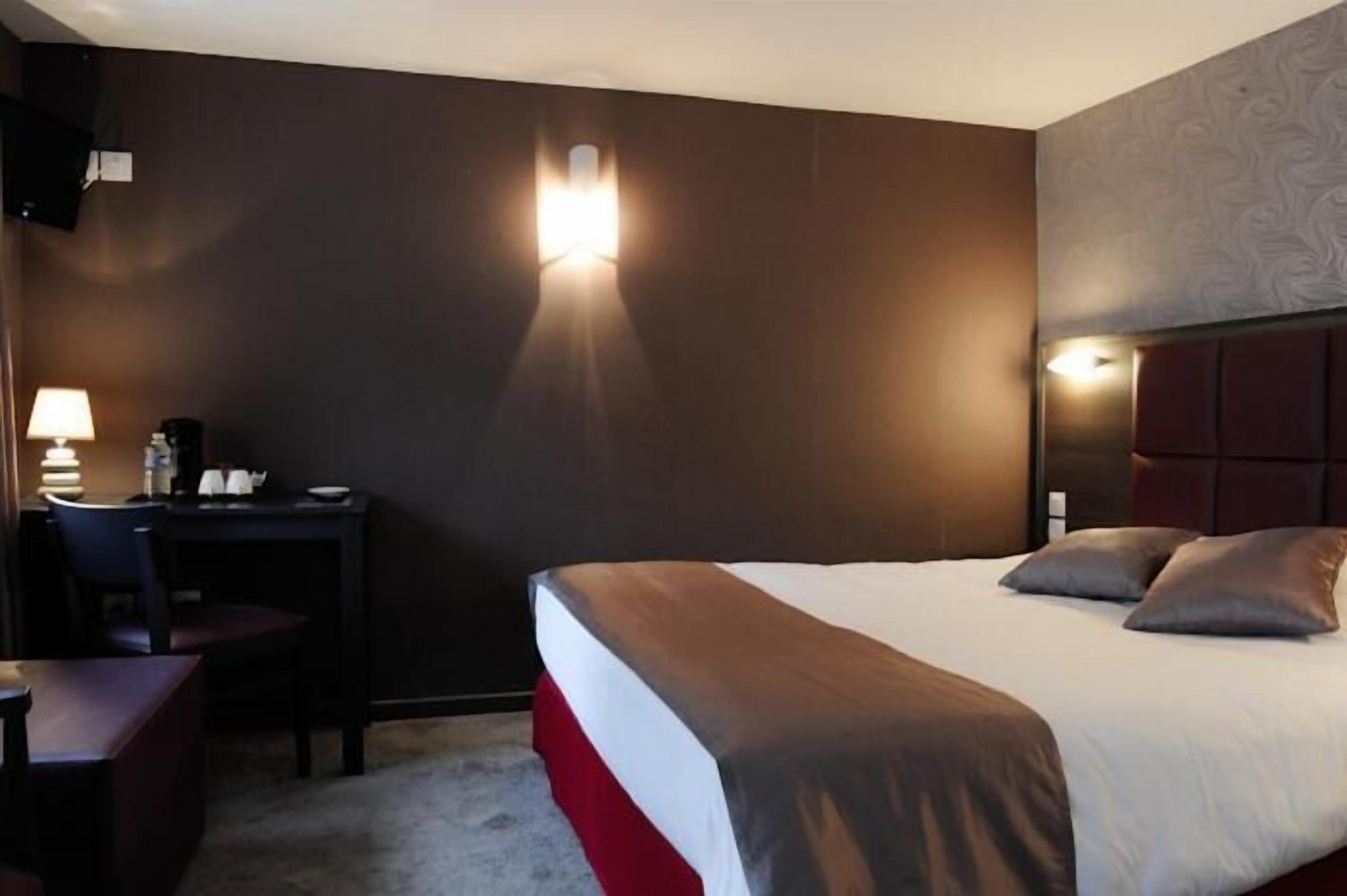 A hotel room with a bed, a desk, and a chair. There are wall sconces providing light.