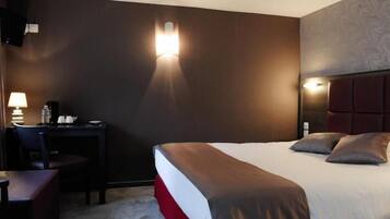 A hotel room with a bed, a desk, and a chair. There are wall sconces providing light.