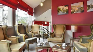 A room with four upholstered chairs, a coffee table, and a red carpet. There are three paintings on the wall and a staircase in the background.