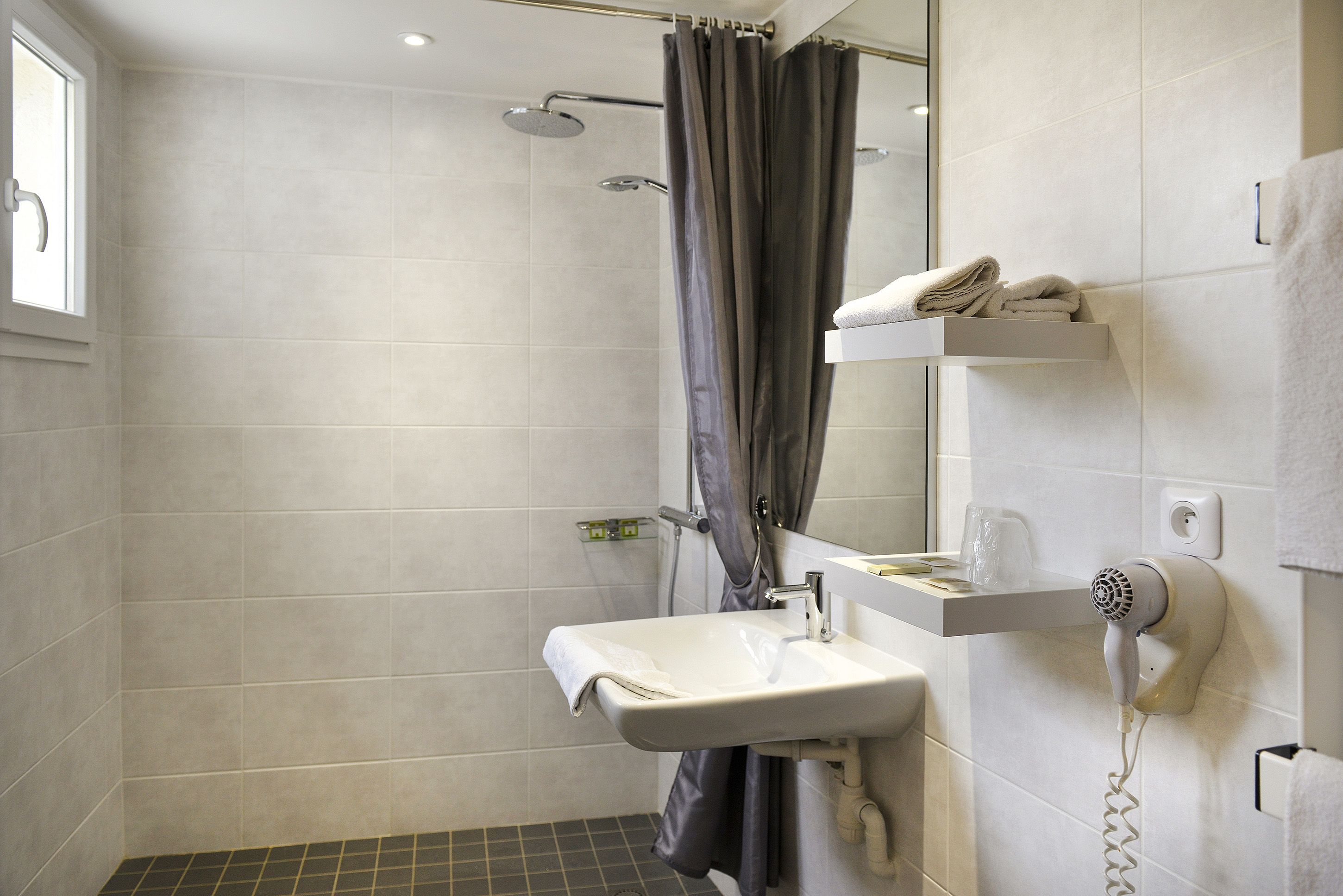 A modern bathroom with a shower, a sink, and a hairdryer mounted on the wall.