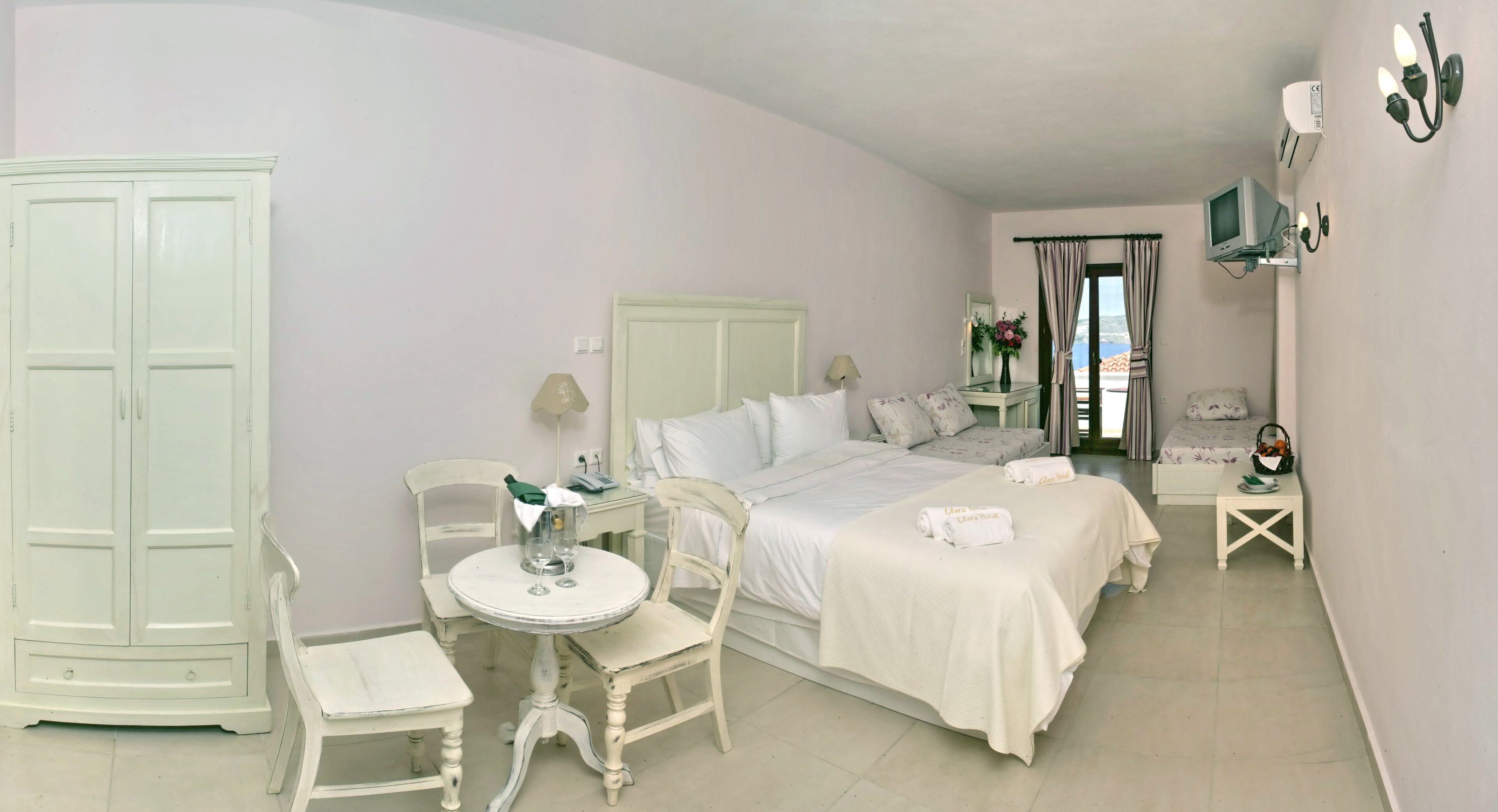 Un dormitorio con cama, mesitas de noche, una silla, un armario y una pequeña mesa con lámpara y jarra.