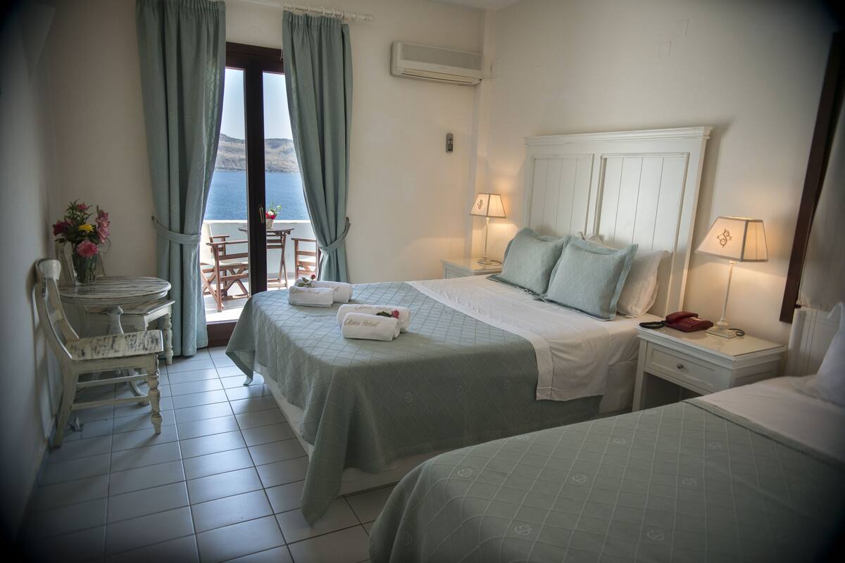 A hotel room with two beds, a balcony with a table and chairs, and a view of the sea.