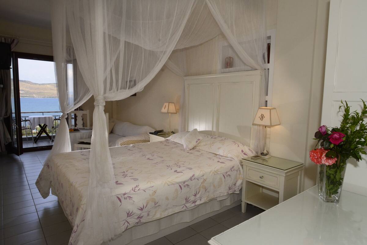 A bedroom with a canopy bed, a bedside table with a lamp, a nightstand, and a vase with flowers.