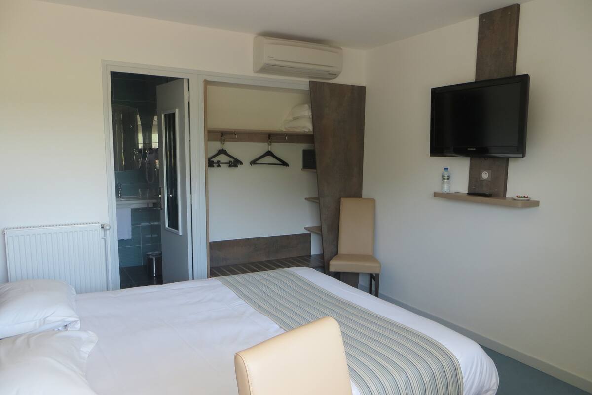 Une chambre d’hôtel avec un lit, une chaise, un téléviseur fixé au mur et une armoire contenant des vêtements.