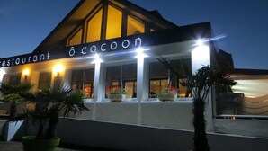 Un restaurant appelé « O cocoon », doté d’un design moderne, avec de grandes fenêtres et des plantes en pot devant l’entrée.