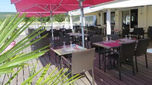Un espace de restauration en plein air, avec des tables et des chaises placées sous des parasols rouges, offrant une vue sur un paysage pittoresque.