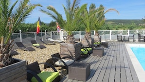 Un espace aménagé au bord de la piscine, avec des chaises longues, des jardinières, des drapeaux et une vue sur le paysage.