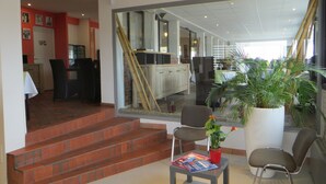 Un espace d’accueil avec un escalier menant à un deuxième étage, un comptoir d’accueil, un coin salon avec des magazines et une grande fenêtre donnant sur l’intérieur.