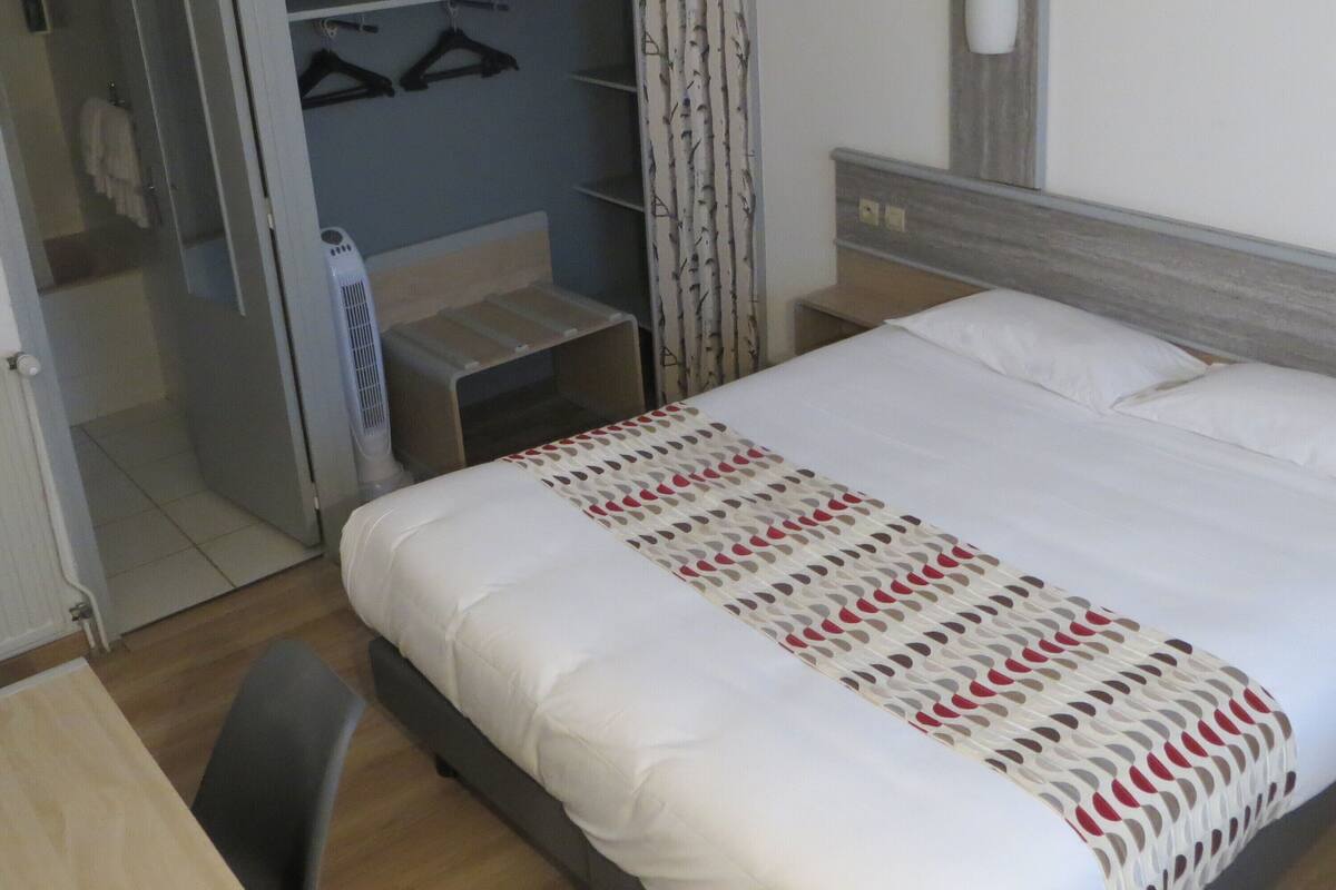Une chambre à coucher comprenant un lit, un bureau, une chaise, une armoire et un miroir.