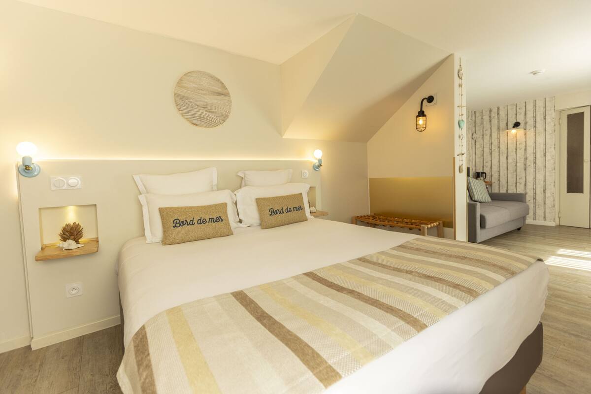 Une chambre avec un grand lit, deux tables de chevet, un luminaire fixé au mur et une vue sur un balcon.
