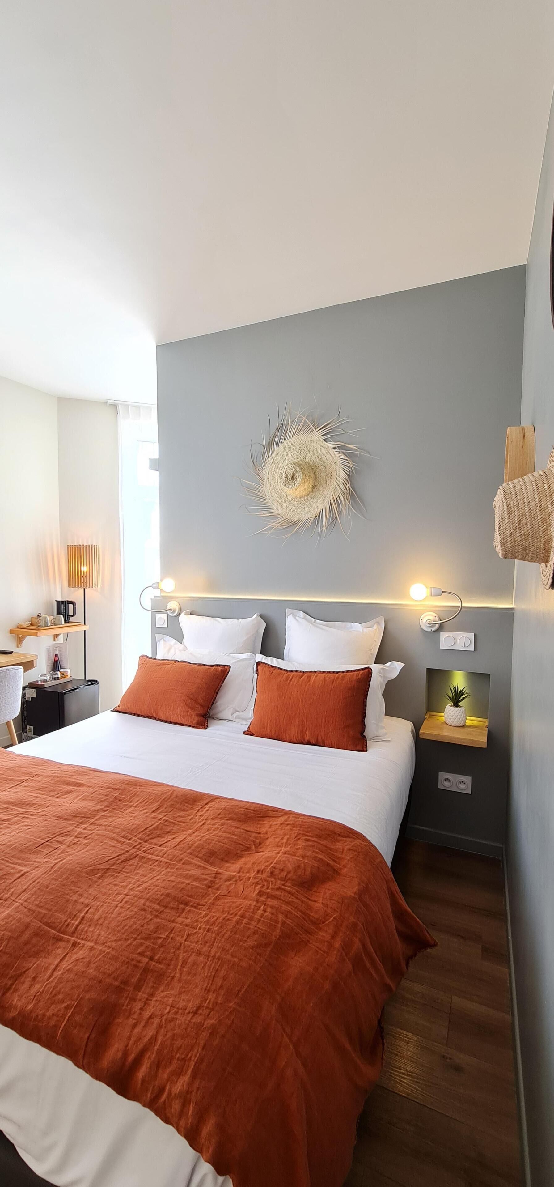 A neatly made bed with white and orange bedding, a wall-mounted decorative item, and a bedside table with a small plant.