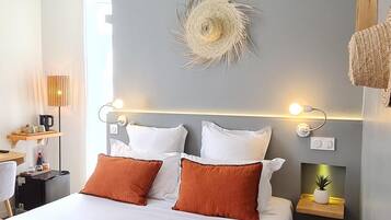 Ein ordentlich bezogenes Bett mit weißer und orangefarbener Bettwäsche, ein an der Wand befestigtes Dekorationsstück und ein Nachttisch mit einer kleinen Pflanze.