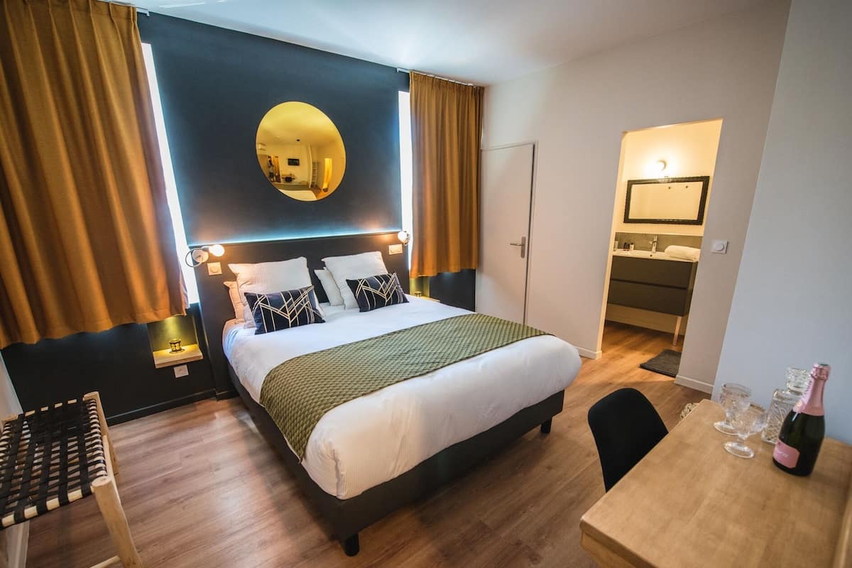 Une chambre d’hôtel équipée d’un lit, d’un bureau, d’une chaise, d’un miroir et d’un mini-bar.