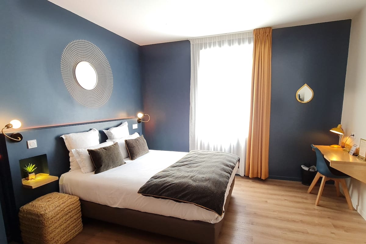 Une chambre moderne avec un grand lit, des tables de chevet avec des lampes, un bureau avec une chaise et une grande fenêtre avec des rideaux.