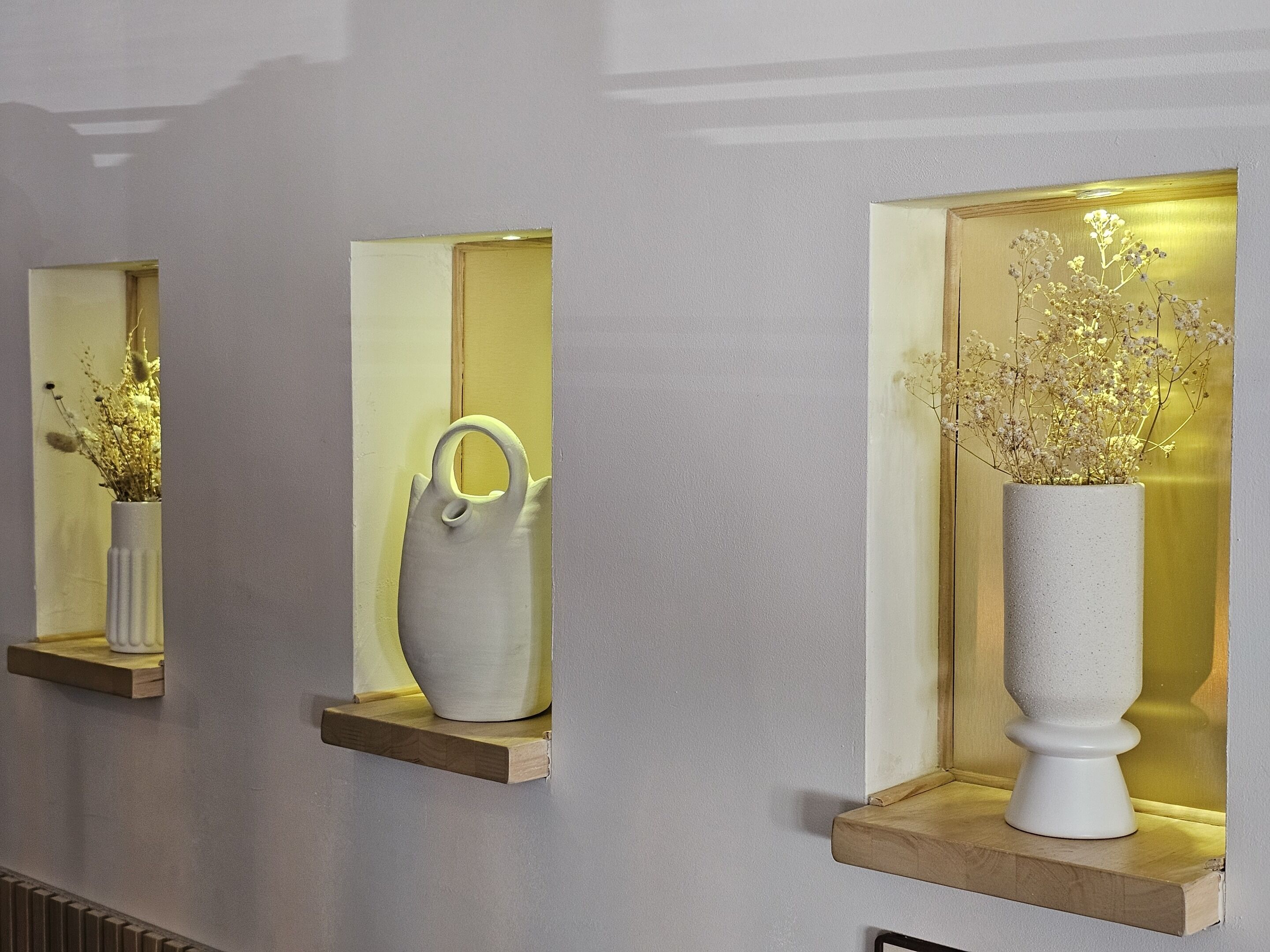 Three wall-mounted shelves with vases containing dried flowers.