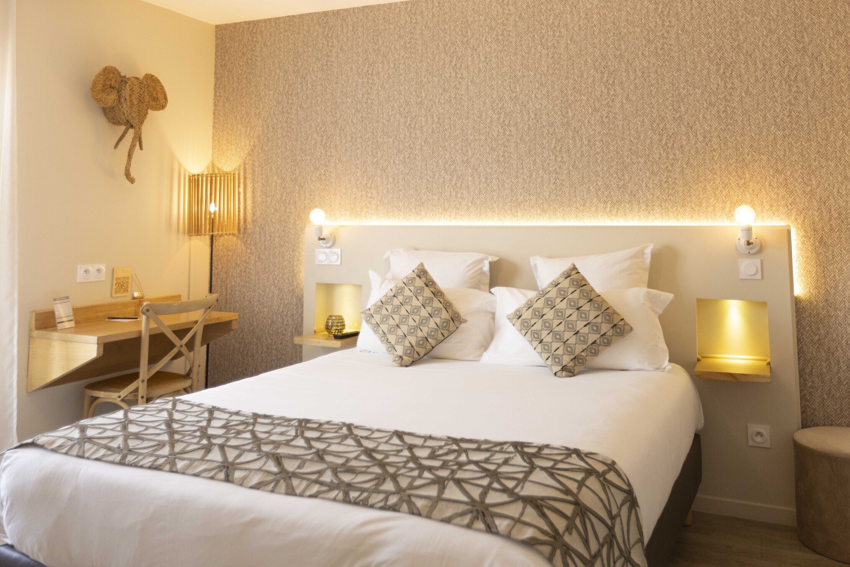 Habitación de hotel con una cama grande, dos lámparas de noche, un escritorio con silla y un objeto decorativo en la pared.