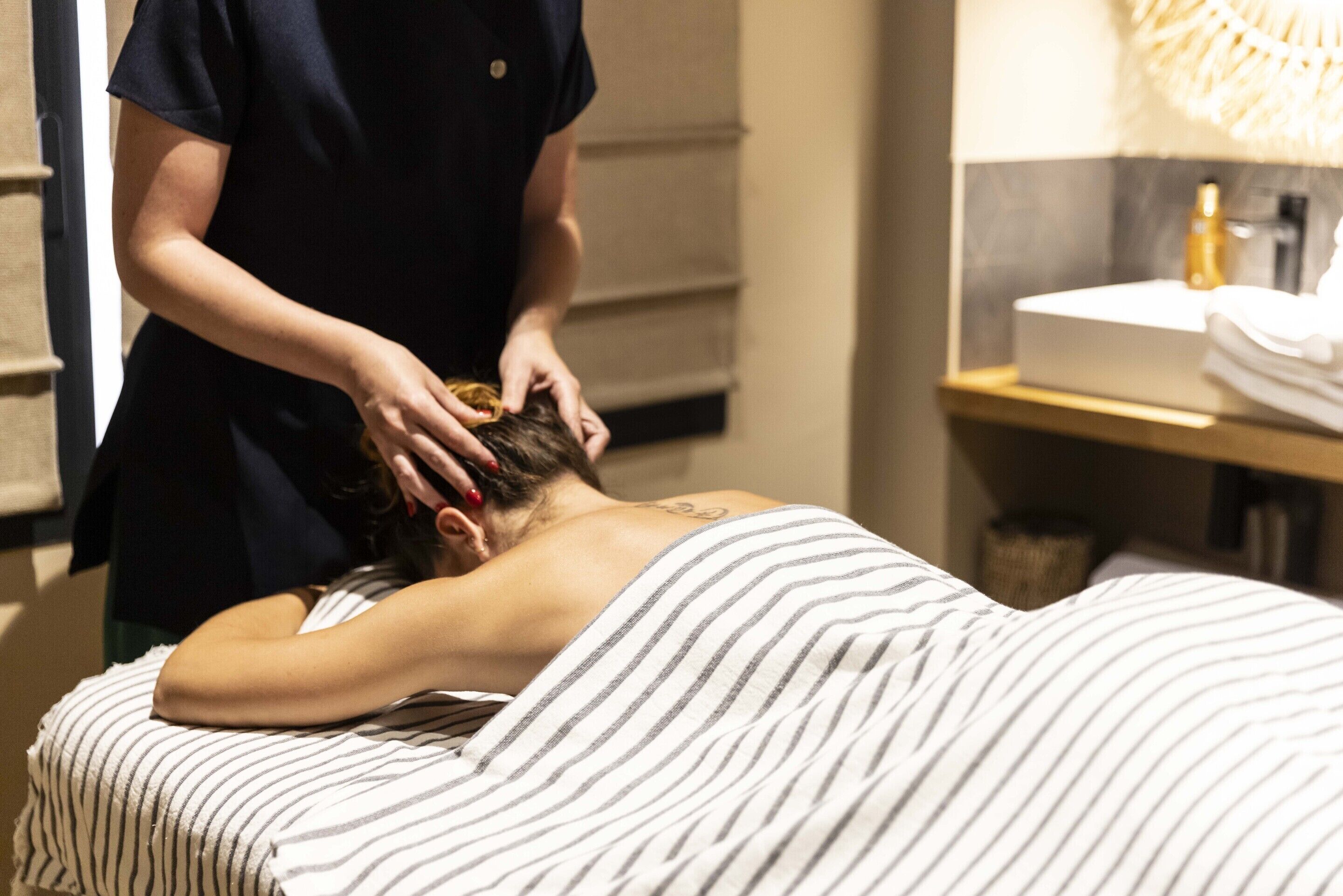 Eine Person erhält eine Massage in einem Raum mit einer gestreiften Bettdecke, einem Waschbecken und einem Handtuchhalter.