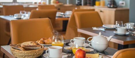 A breakfast setting with tables, chairs, and a variety of breakfast items including bread, juice, and eggs.