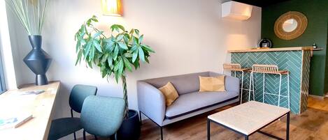 Un espacio moderno con sala de estar, sofá, sillas, una mesa de centro, una planta en maceta y una lámpara de pared.