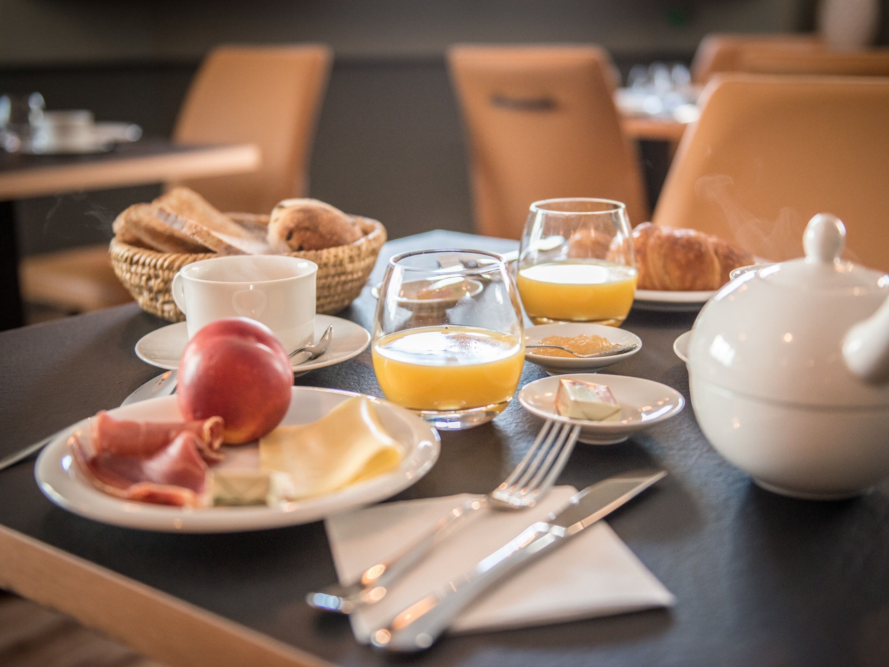 Une table de petit-déjeuner dressée avec des assiettes remplies de nourriture, des verres de jus d’orange, une théière et des couverts.