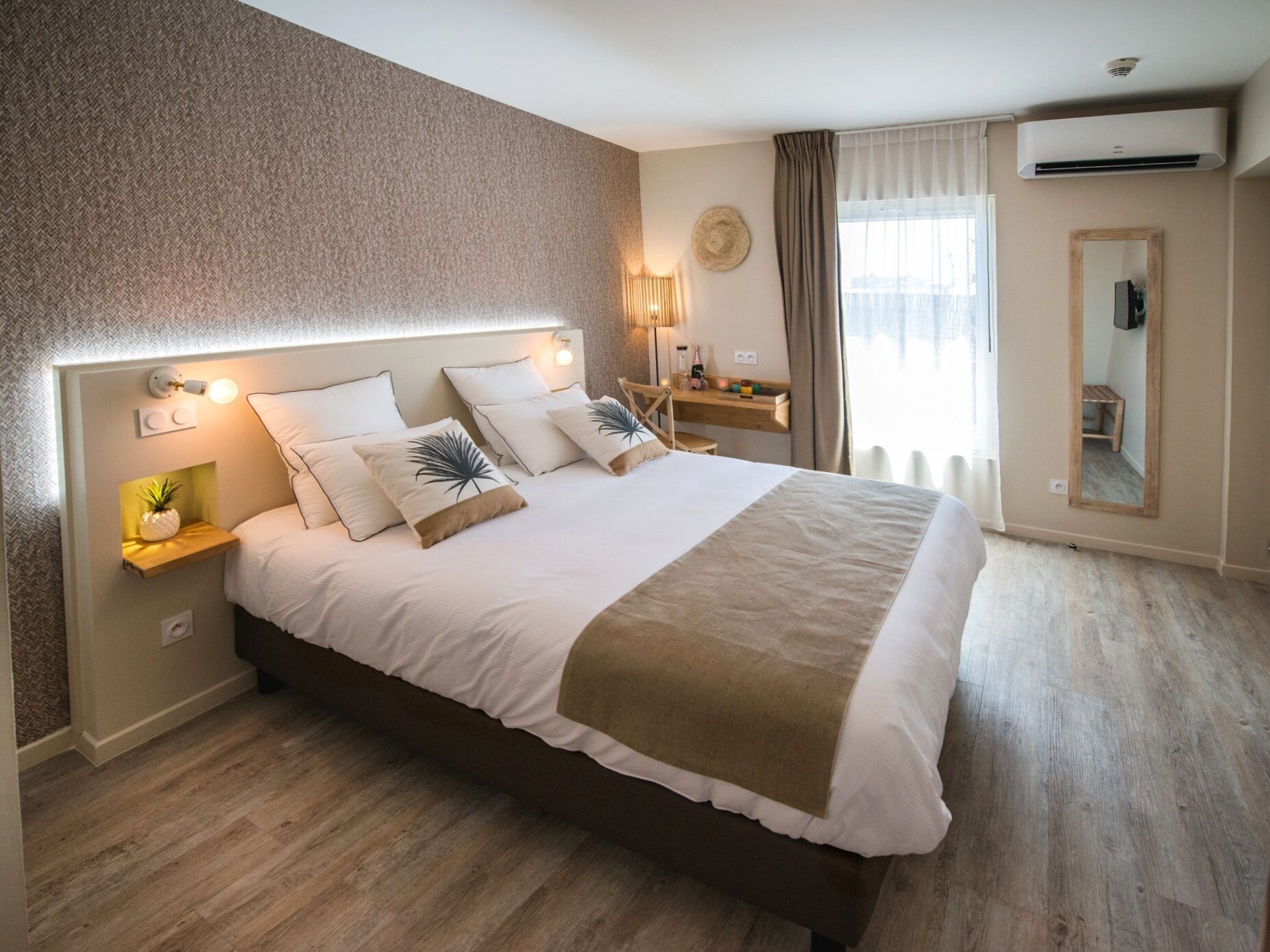 A modern bedroom with a large bed, bedside tables, a desk, and a mirror.