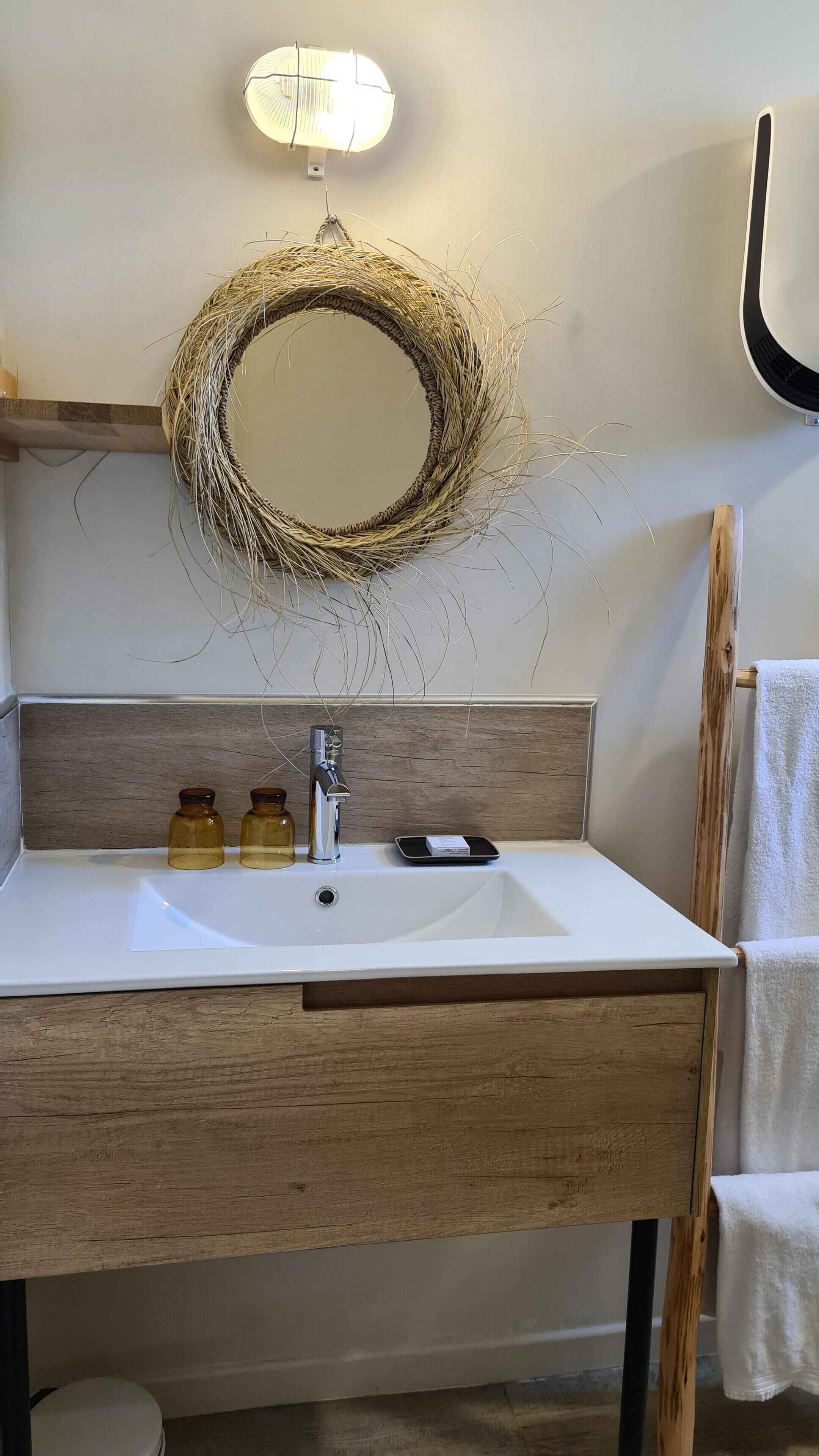 Un baño con un lavabo blanco, dos botellas ámbar, un grifo plateado y un espejo con marco trenzado.