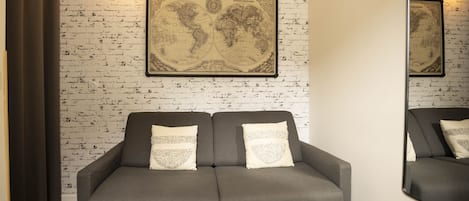 Un sofá gris con almohadones decorativos frente a una pared con estampado de ladrillo y un mapa mundial enmarcado.