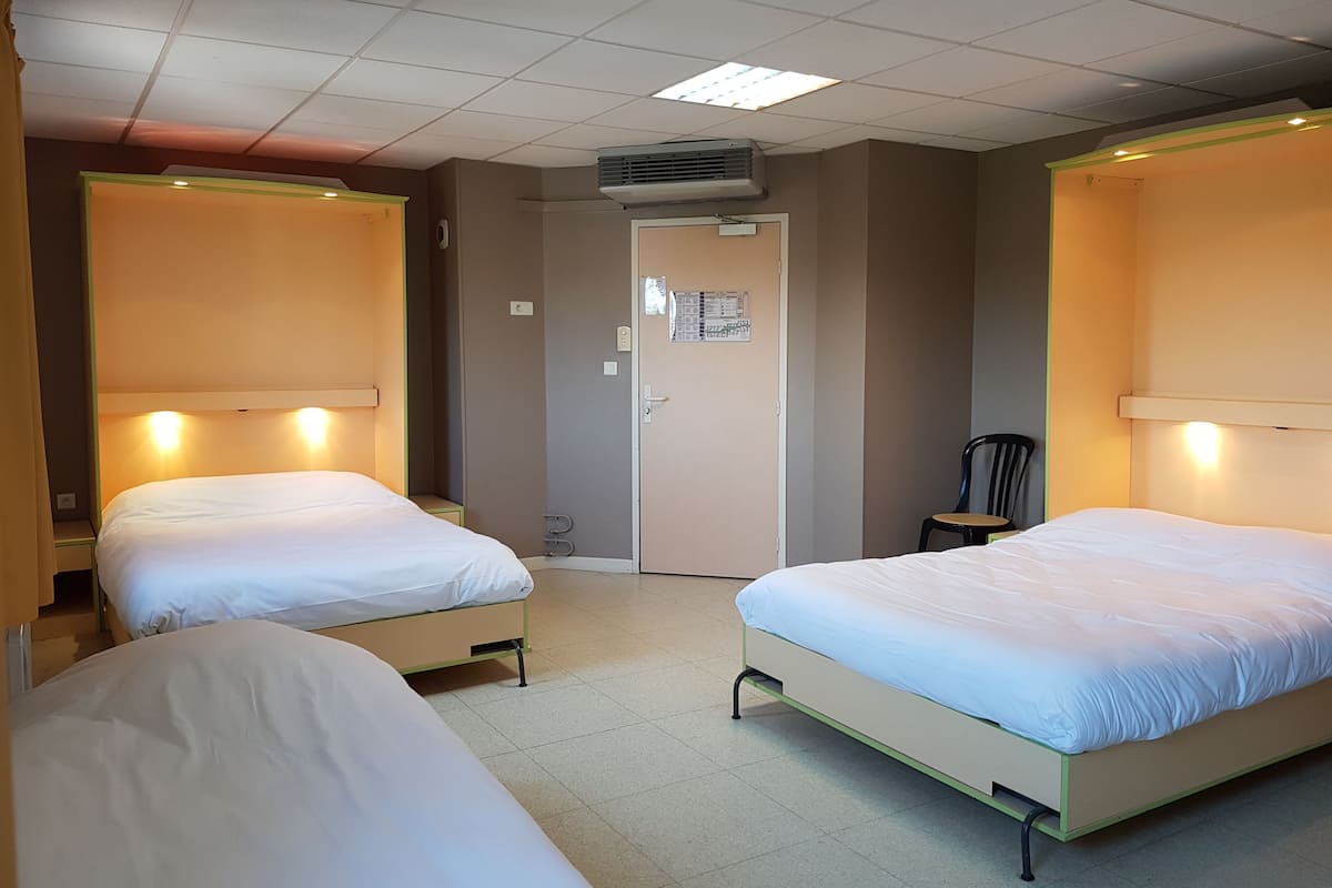 A hotel room with two single beds, a door, and an air conditioning unit on the ceiling.