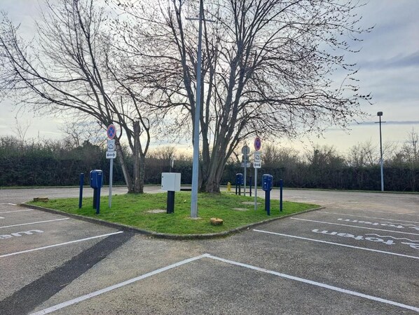 Un estacionamiento con espacios delimitados y una isla central con árboles y un cartel.