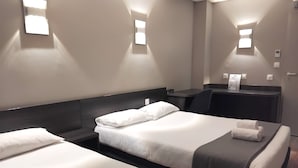 Et hotelværelse med to senge, et skrivebord og en stol. Væglamper og termostat er monteret.