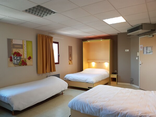 A hotel room with two single beds, a window with curtains, a wall-mounted air conditioner, and a door with a sign.