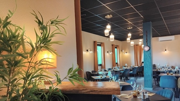 En restaurant med dækketøjsbestykket borde, en trædisk og hængende pendellamper.
