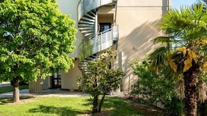 En moderne bygning med en spiraltrappe, omgivet af velholdt beplantning og en anlagt sti.