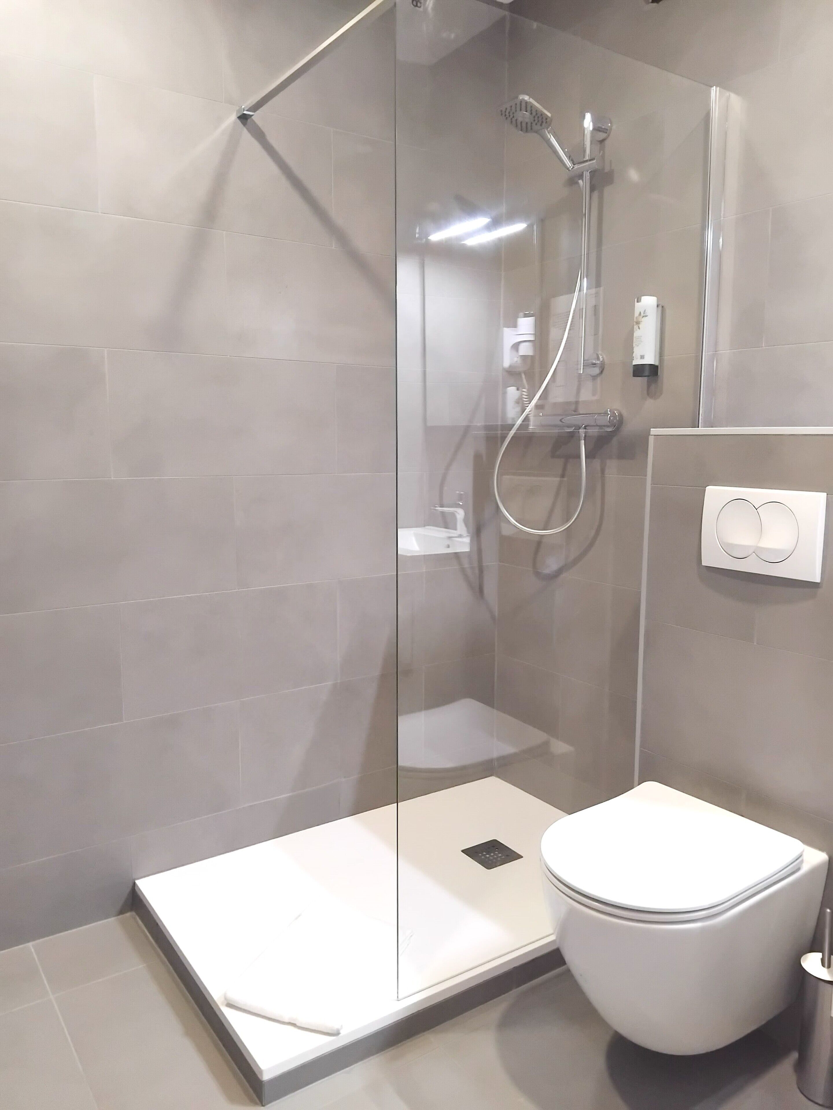 A modern bathroom with a glass-enclosed shower, a white toilet, and a wall-mounted hand dryer.