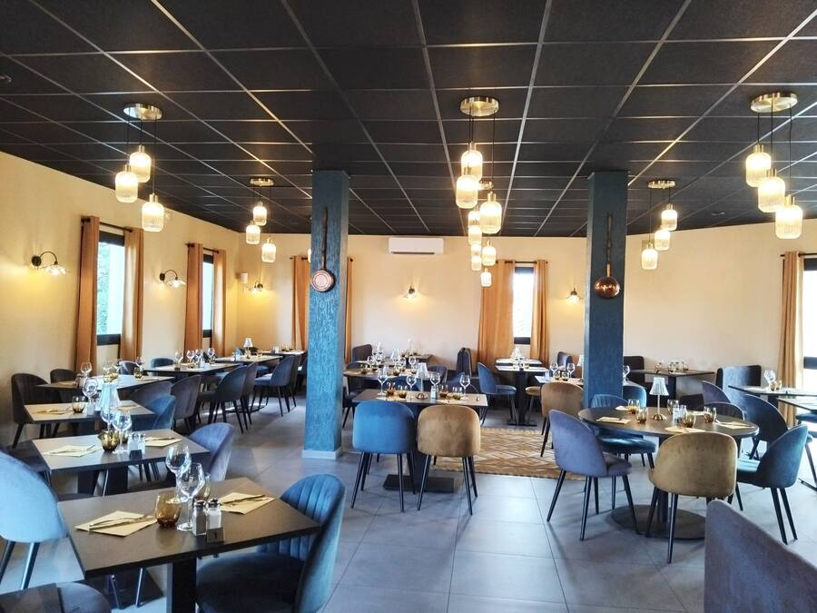 A restaurant with multiple tables and chairs, ceiling lights, and a large pillar.