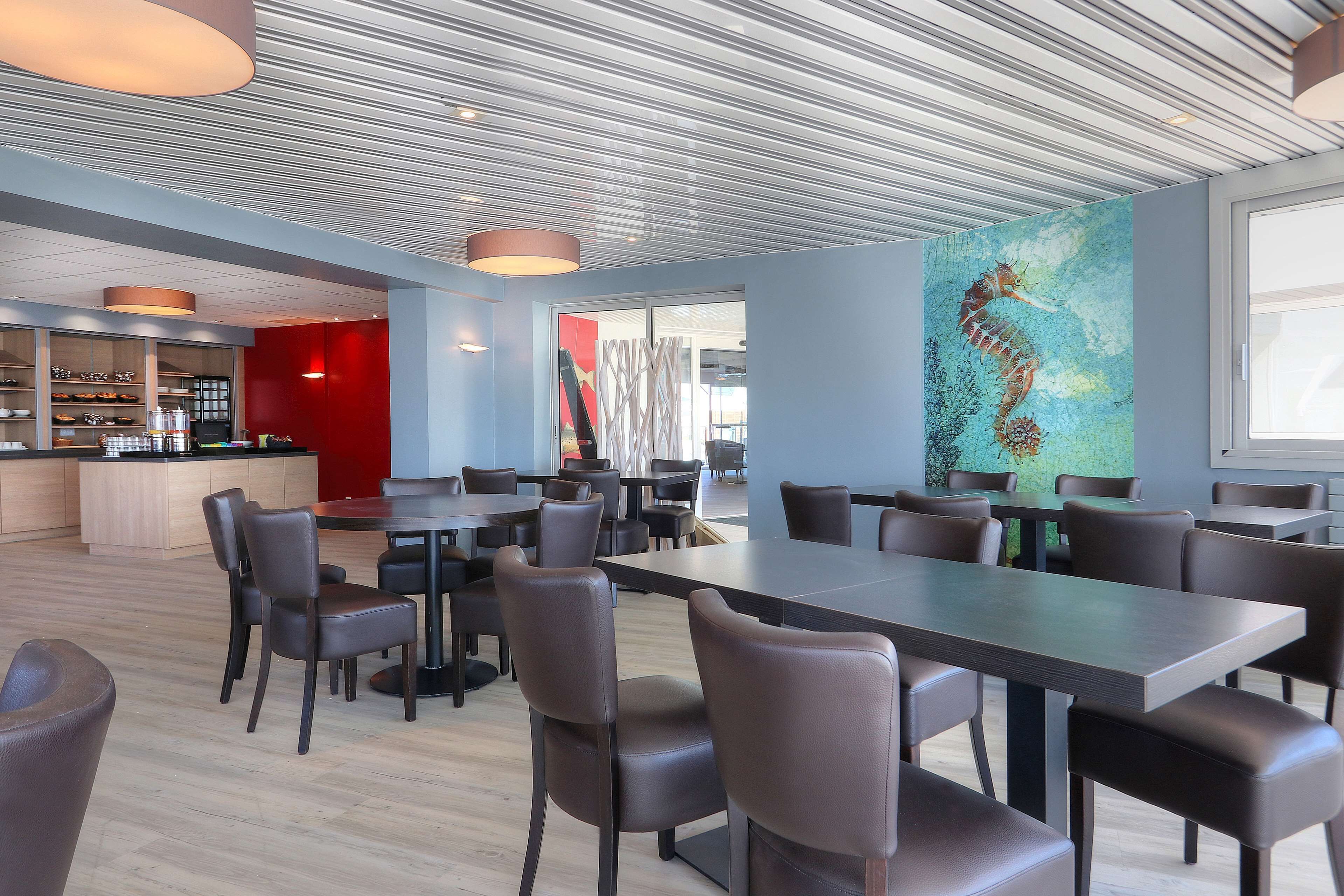 A modern dining area with a long table and chairs, a bar area with shelves, and a large seahorse mural on the wall.