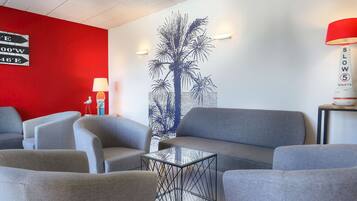 A modern lounge area with grey sofas and armchairs, a glass coffee table, and a red accent wall.