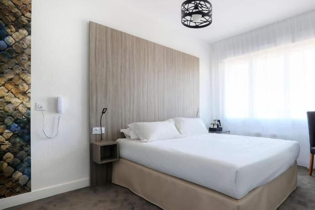 Quarto de hotel com cama, escrivaninha, cadeira, televisão e parede de pedra.