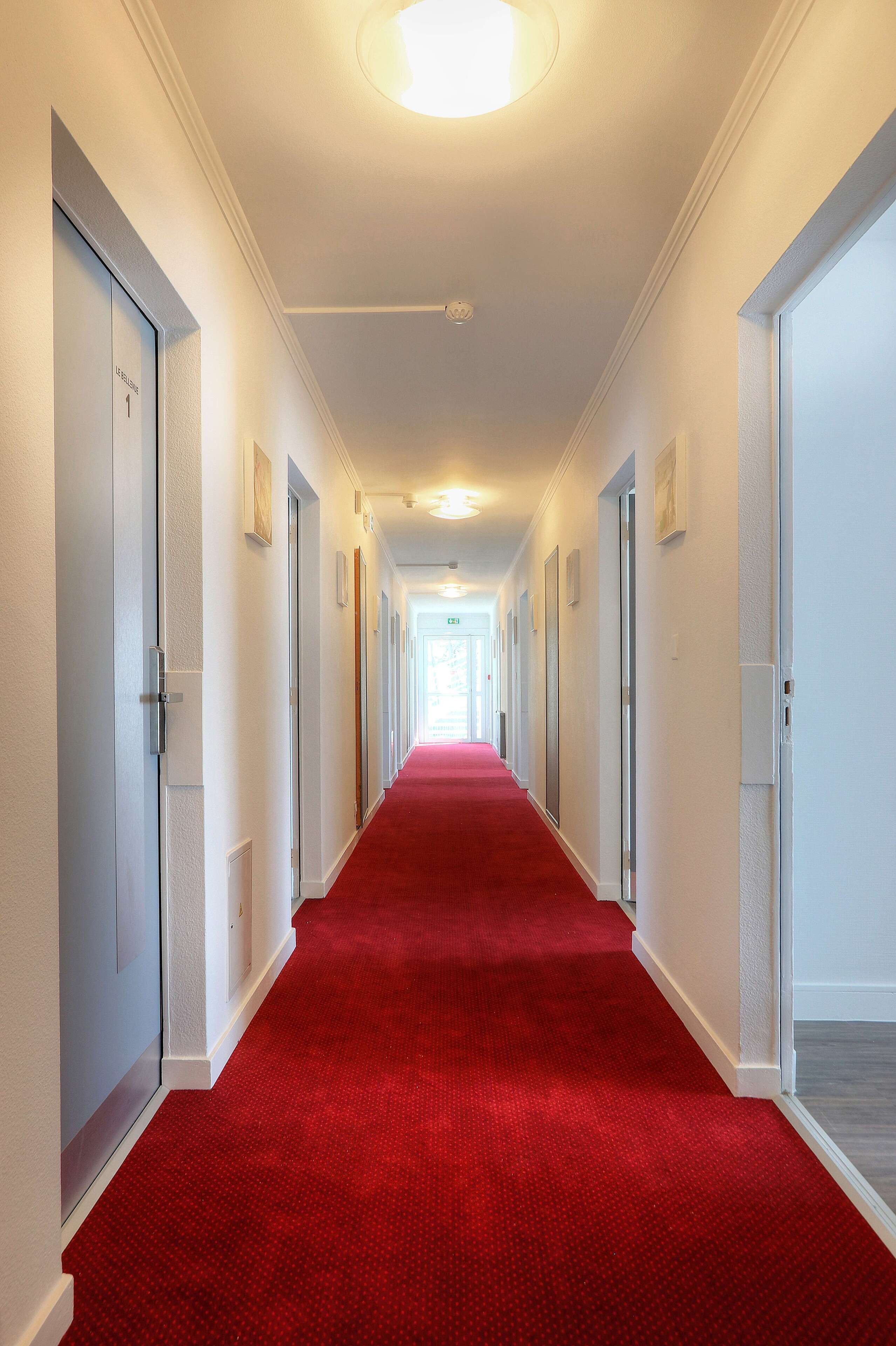 A long hallway with red carpet, white walls, and doors on both sides.