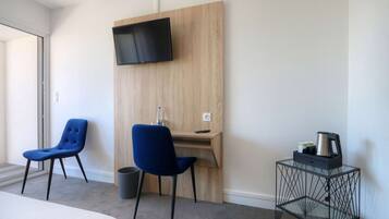 Habitación de hotel con cama, dos sillas azules, un escritorio de madera con televisor, cafetera y cesto de basura.