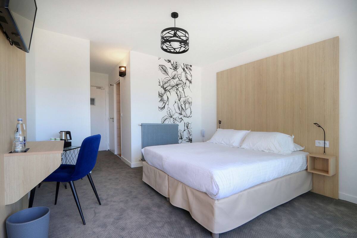 Quarto de hotel moderno com cama, escrivaninha, cadeira e prateleira na parede.
