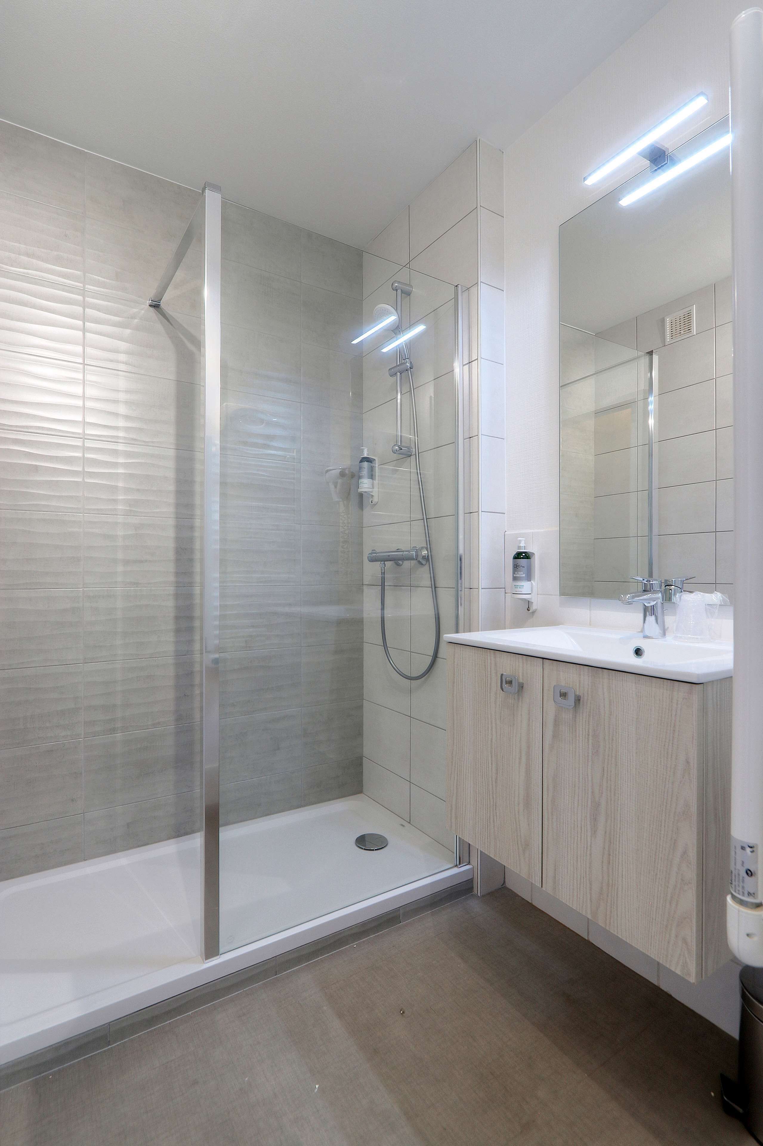 Une salle de bain moderne avec une douche à parois de verre, un lavabo blanc et des meubles en bois.