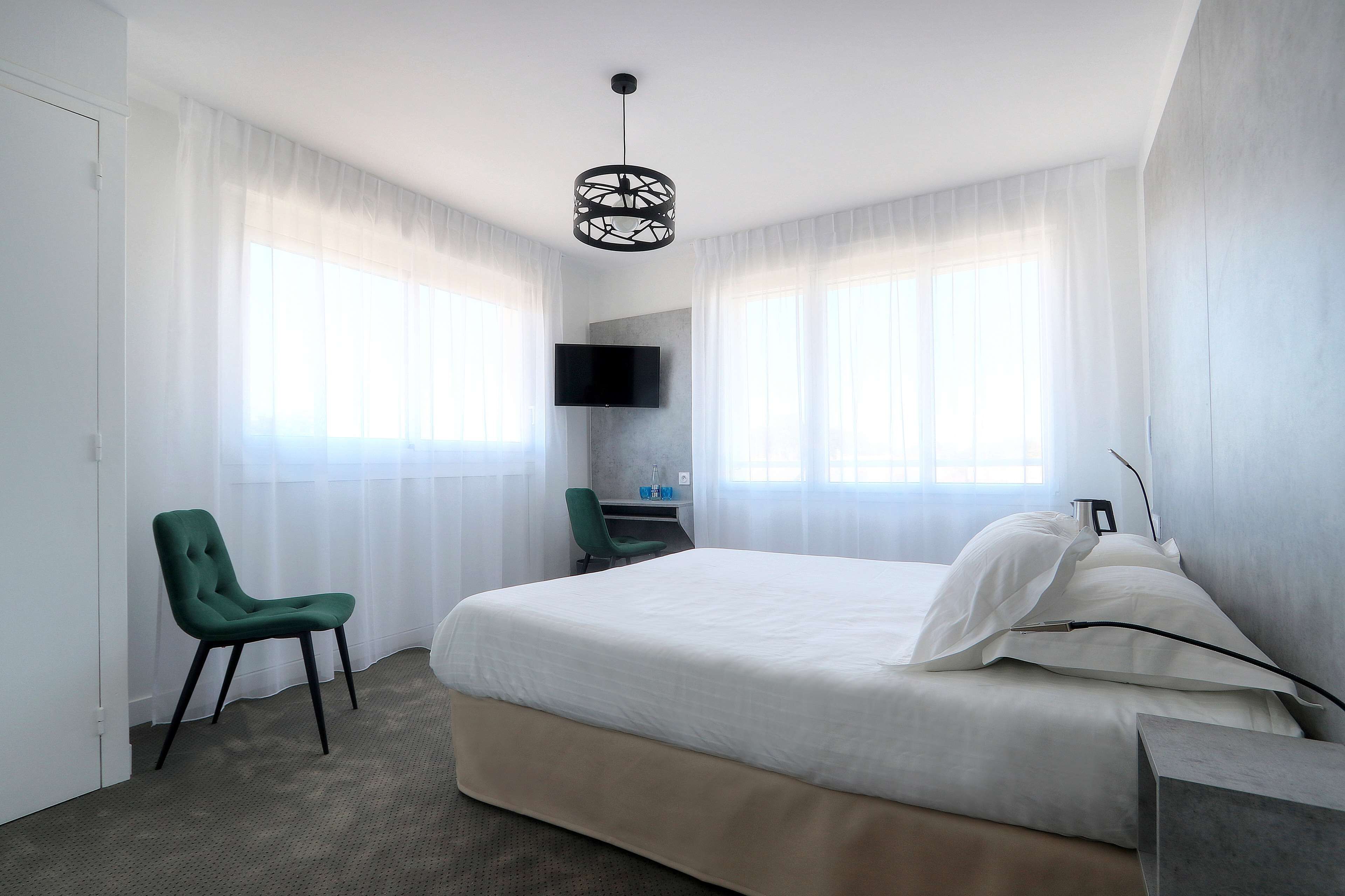A hotel room with a bed, a desk, a chair, a TV, and a window with curtains.