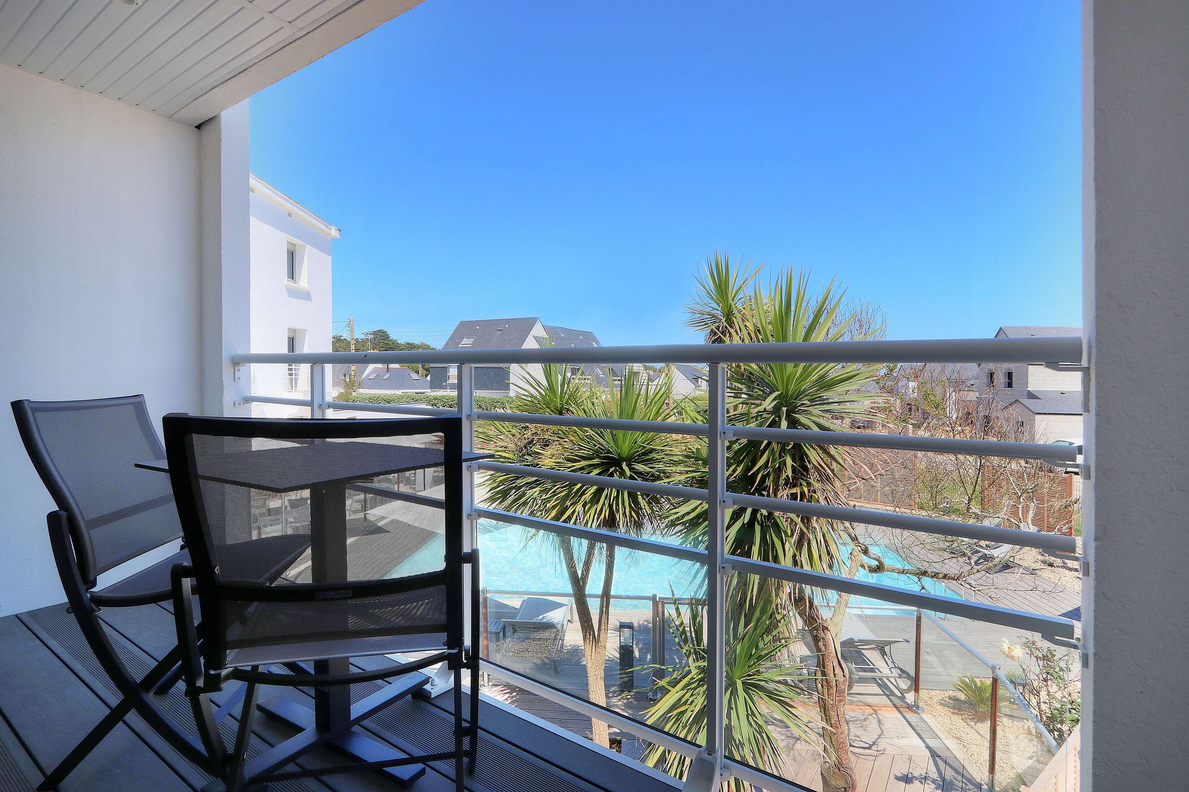 A balcony with a table and chairs, overlooking a swimming pool and palm trees.
