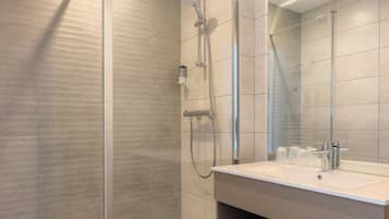 Une salle de bain moderne avec une douche à parois de verre, un lavabo avec un miroir et une poubelle.