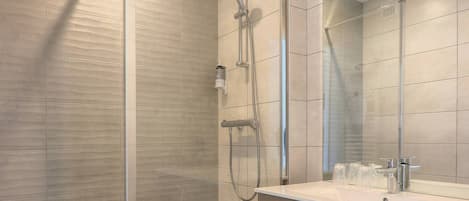 A modern bathroom with a glass-enclosed shower, a sink with a mirror, and a trash bin.