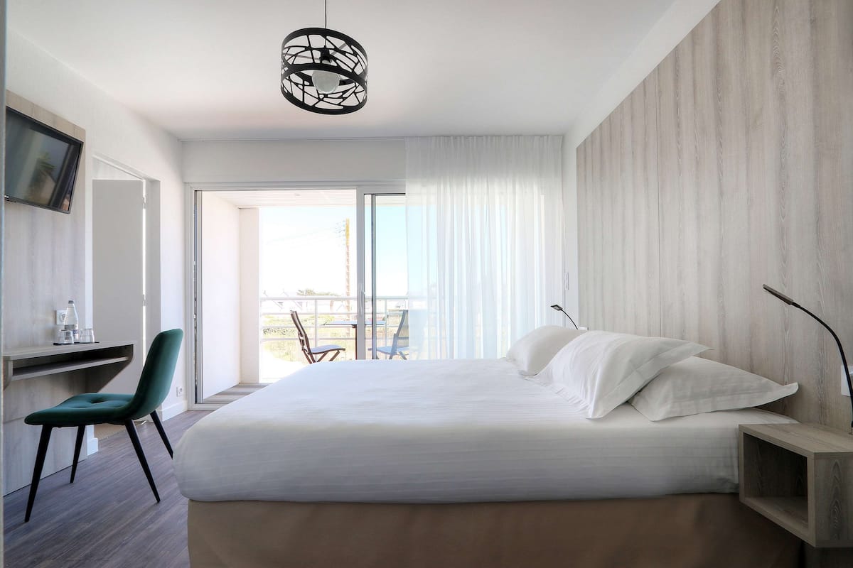 Quarto moderno com uma cama grande, uma escrivaninha e uma cadeira. Possui uma varanda com vista.