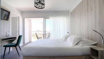 A modern bedroom with a large bed, a desk, and a chair. There is a balcony with a view.
