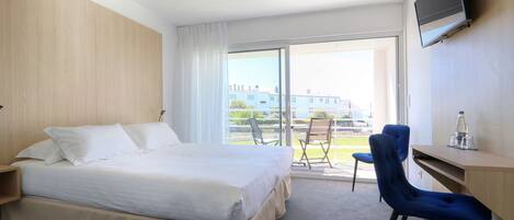 Habitación de hotel con cama, escritorio, silla, televisión y balcón con vistas a edificios.